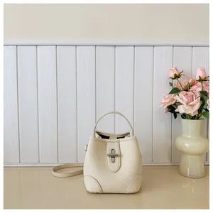 Detail of cream bucket bag in pebble leather with silver twist lock and slim shoulder strap