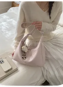 Detail of pink pleated hobo bag featuring a plush ball charm and adjustable shoulder strap