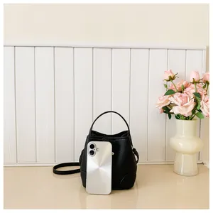 Close-up of black grainy leather bucket bag with top handle and silver phone for scale