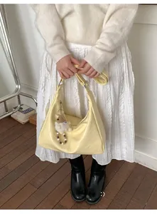 Detail of light yellow crescent tote bag with a cute brown bear plush charm on strap