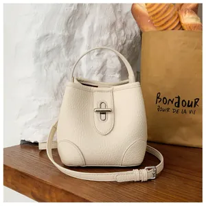 Detailed view of cream bucket bag with lychee grain texture and silver metal twist lock