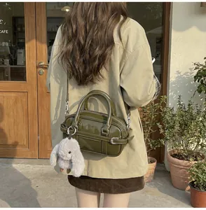 Outdoor shot of deep olive green PU leather handbag with a plush bunny charm on a model