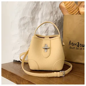 Detail of yellow lychee leather bucket bag with silver turn-lock on wood surface