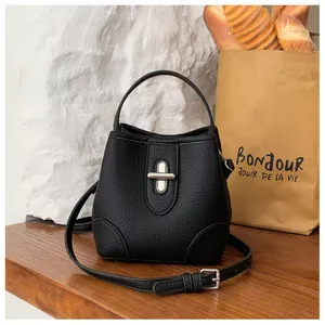 Detail of black pebbled leather bucket bag with silver oval twist lock on a wooden table