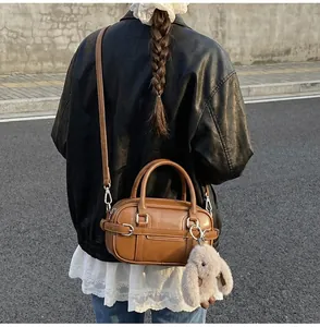 Outdoor shot of a brown vintage leather bowling bag with a plush bunny charm and shoulder strap