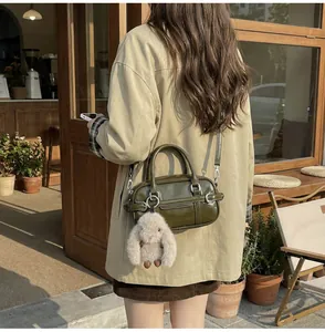 Olive green mini Boston bag with plush bunny charm worn by model in a trench coat