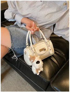 Detail einer beigen Boston-Tasche mit Metallschloss und süßem Hundeanhänger auf Sofa