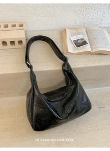 Detail of black glossy patent leather hobo bag with silver buckle on stone background