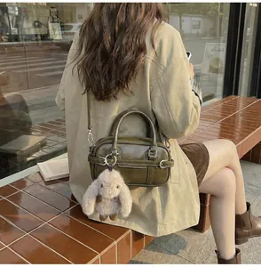 Olive green bowling bag with leather texture and cute rabbit charm on a park bench