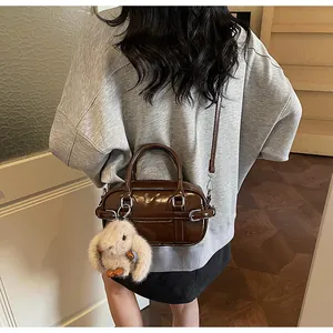 Detailed side view of a brown leather bowling bag with a plush rabbit charm accessory