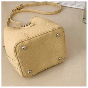 Detailed view of the creamy yellow leather bucket bag with silver base studs and grainy texture