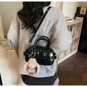 Detail of a black glossy bowling bag with a beige plush rabbit charm on a long strap