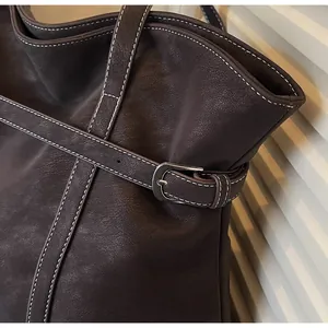 Detail der dunkelbraunen Ledertasche mit weißen Kontrastnähten und silberner Metallschnalle