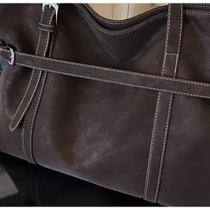 Detailansicht der braunen Ledertasche mit weißen Kontrastnähten und silberner Schnalle