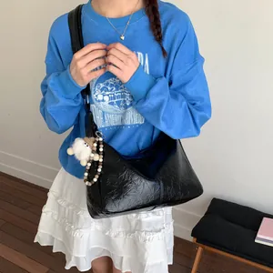 Versatile black leather shoulder tote bag for women with an adjustable strap and pom pom charm