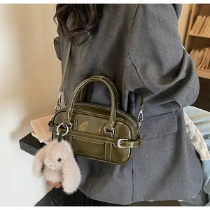 Detail of olive green glossy leather bag with plush rabbit charm on grey blazer