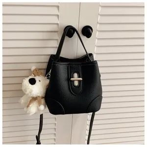 Close-up of black litchi pattern bucket bag with metal lock and cute dog plush charm