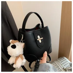 Detail of black pebbled leather bucket bag with metal lock and white plush puppy charm