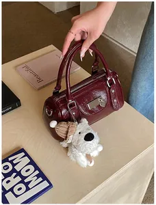 Makro-Detail der weinroten Lackleder-Bowlingtasche mit Silberbeschlägen und Plüschanhänger