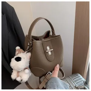 Detail of brown lychee grain bucket bag featuring a silver lock and plush puppy charm