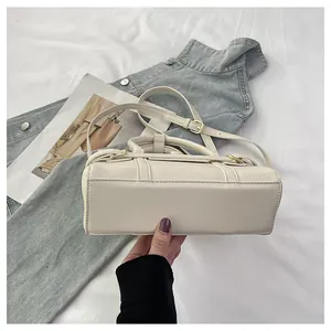 Vue détaillée du bas d'un sac bandoulière blanc crème avec des coutures précises