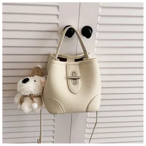 Close-up of off-white bucket bag with silver clasp and plush dog charm on a door