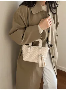 Detail of cream crossbody bag with wave texture and leather tassel on a khaki coat