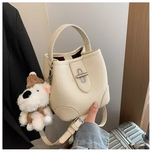 Detail of cream bucket bag showing lychee leather texture, silver lock, and plush puppy charm