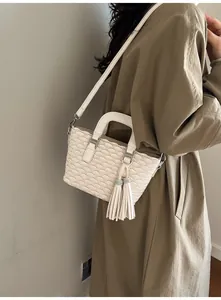 Detail of cream crossbody bucket bag featuring scalloped embossing and tassel accent