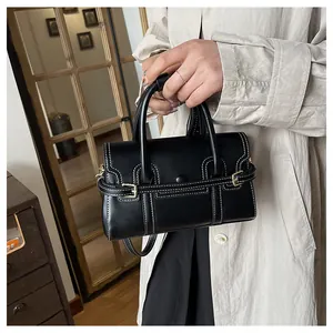 Détail d'un sac à main noir en similicuir avec surpiqûres blanches et ferrures dorées