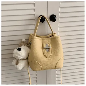 Detail of yellow lychee leather bucket bag with silver turn-lock and plush puppy charm
