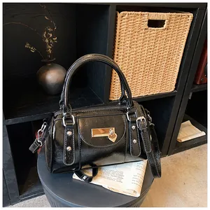 Detail der schwarzen glänzenden Boston-Tasche mit Herzanhänger und verstellbarem Gurt