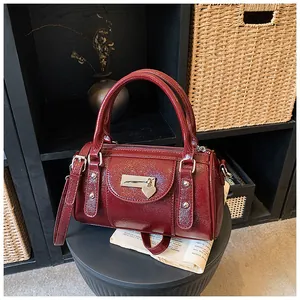 Detail der burgunderroten glänzenden Boston-Tasche mit silbernem herzförmigem Metallanhänger