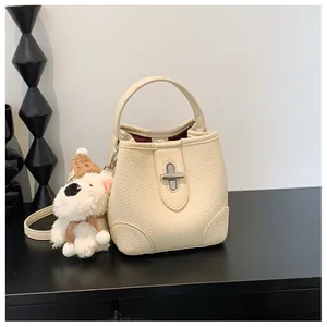 Detail of cream bucket bag showing lychee grain leather, metal lock, and puppy charm