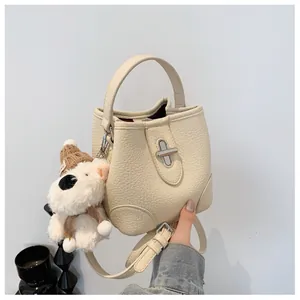 Detail of cream bucket bag showing lychee grain leather and plush dog charm with silver buckle