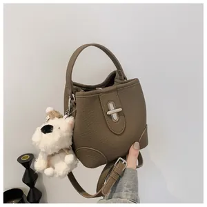 Close-up of brown litchi leather bucket bag with cute plush puppy charm and silver buckle