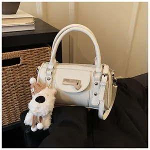 Weiße Boston-Tasche mit Herzanhänger, Plüschhund und verstellbarem Gurt auf dunklem Stoff