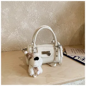 Detail einer weißen Boston-Tasche mit flauschigem Welpen-Anhänger und Herz-Medaillon