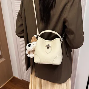 Minimalist cream leather bucket bag with dog pendant shown on a model's shoulder