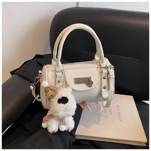 Detailansicht der beigen Boston Tasche mit Herzanhänger und Plüschtier auf einem Ledersessel