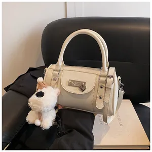 Detail der cremeweißen Zylindertasche mit Lederstruktur und silbernem Herzanhänger