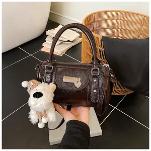 Detail einer braunen Lackleder-Boston-Tasche mit Nieten und einem Plüschhund-Anhänger