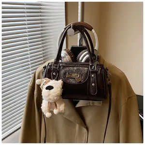 Detail einer dunkelbraunen Bowling-Tasche aus Glanzleder mit Plüschhund-Anhänger