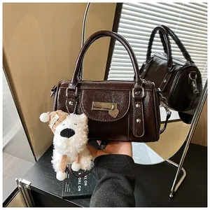 Detail der dunkelbraunen Lackleder-Bowlingtasche mit Herzanhänger und Plüschhund-Anhänger