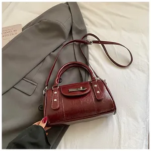 Detailansicht der weinroten Lackleder-Bowling-Bag mit silbernen Nieten auf grauem Sakko