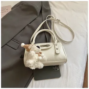 Detail der cremeweißen Kunstledertasche mit Metallschnalle und Teddybär-Anhänger
