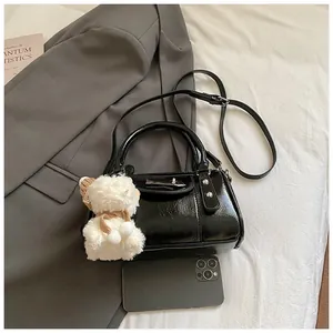 Detail der schwarzen Lack-Pilllow-Bag mit silbernem Schloss und Plüschschaf neben Handy