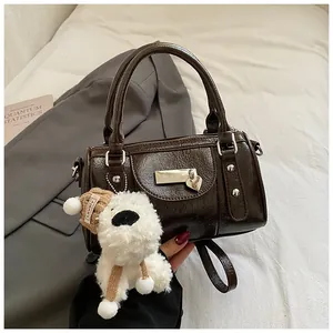Detail einer dunkelbraunen Boston-Tasche mit Plüsch-Anhänger und metallischem Emblem