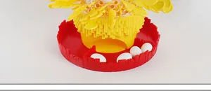 Detail of hen laying egg game showing red base tray with four white toy eggs and yellow funnel