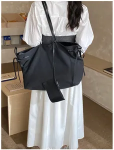 Detail of a large black tote bag with side drawstring and detachable pouch on model